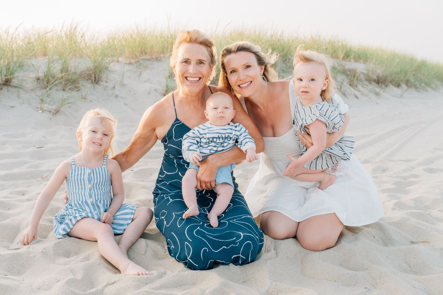 A windy day at the beach with a mother and her daughter's family laugh in the sand.