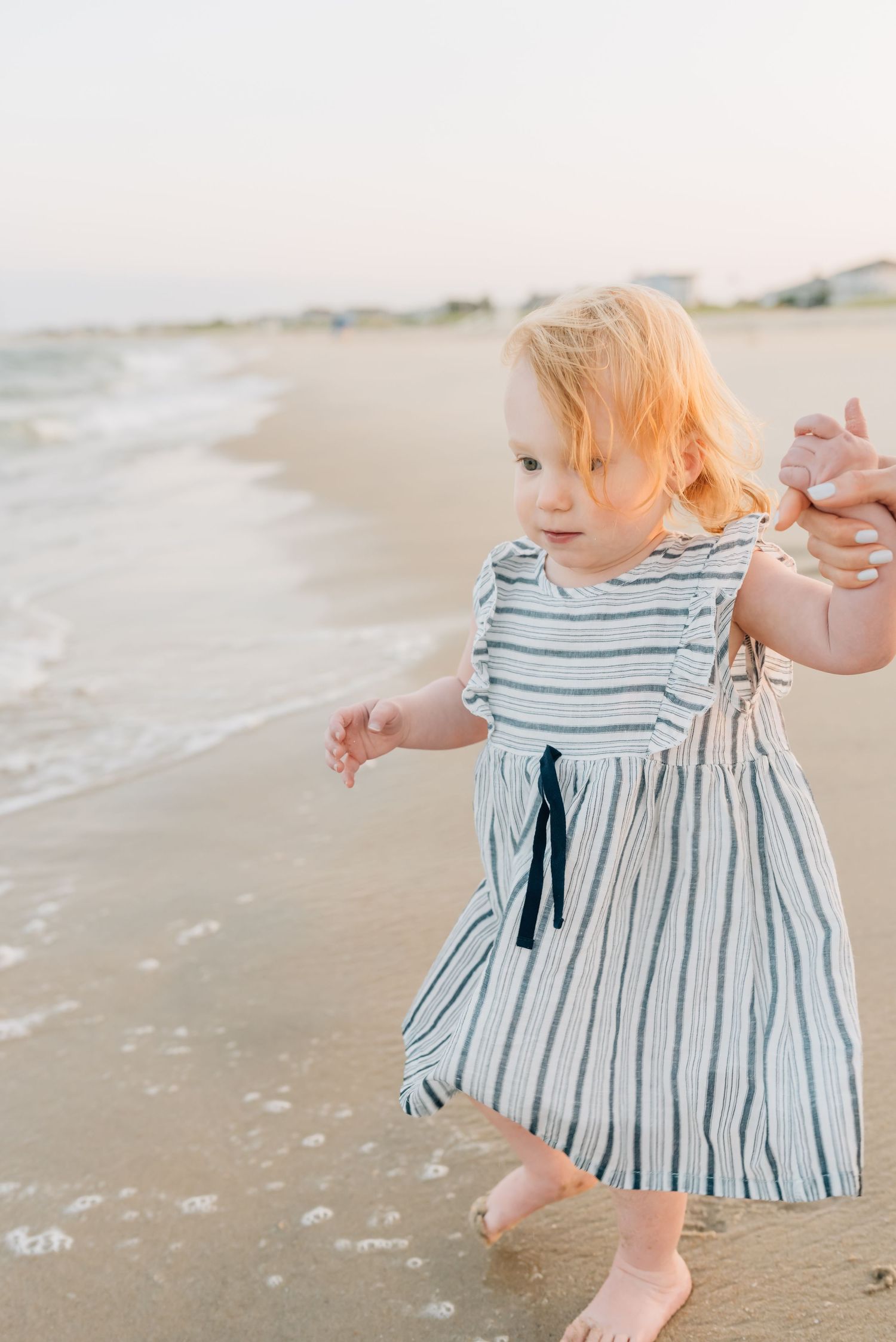 The sun hits the back of a blond young girl as she runs to splash in the ocean at a NJ beach family photo session.