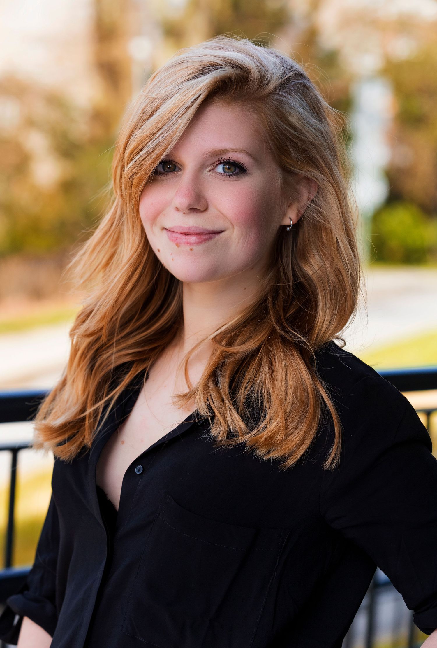 Professional headshot of person with styled hair wearing black blazer against outdoor setting.