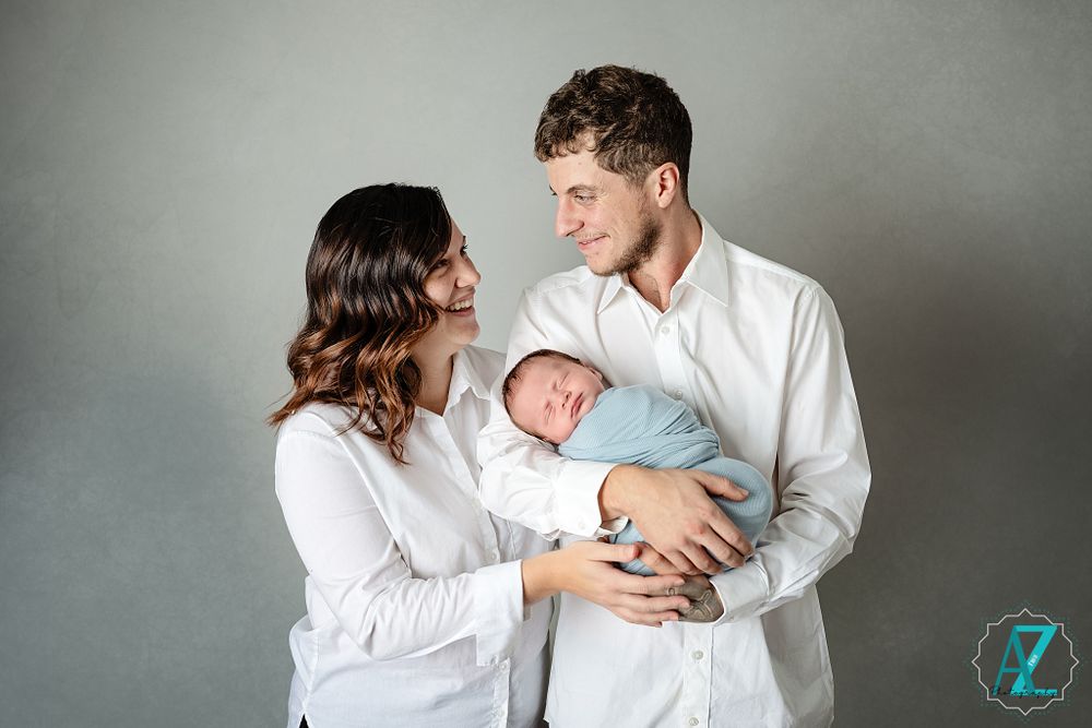 A tender family moment as parents in white shirts gaze at their swaddled newborn.