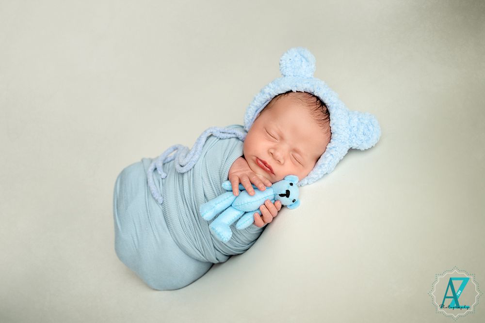 Newborn baby in blue swaddle and bear hat sleeping peacefully on light background.