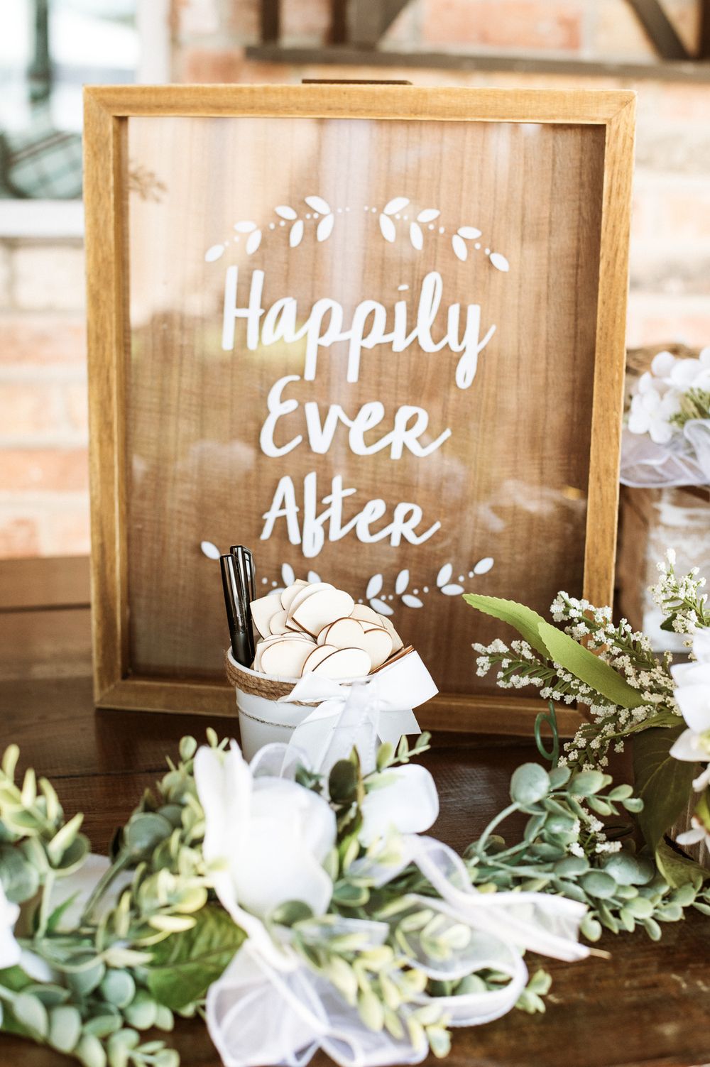 Wooden wedding sign reading 'Happily Ever After' decorated with white flowers and greenery.