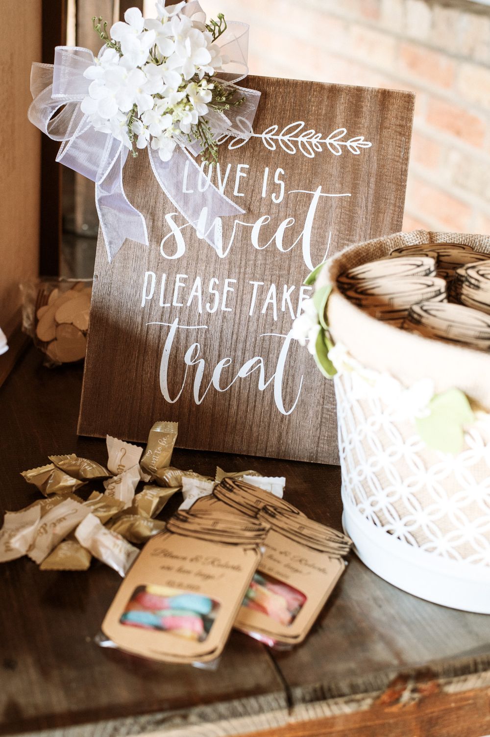 'Love is Sweet' wooden wedding sign with treat bags and white floral decor.