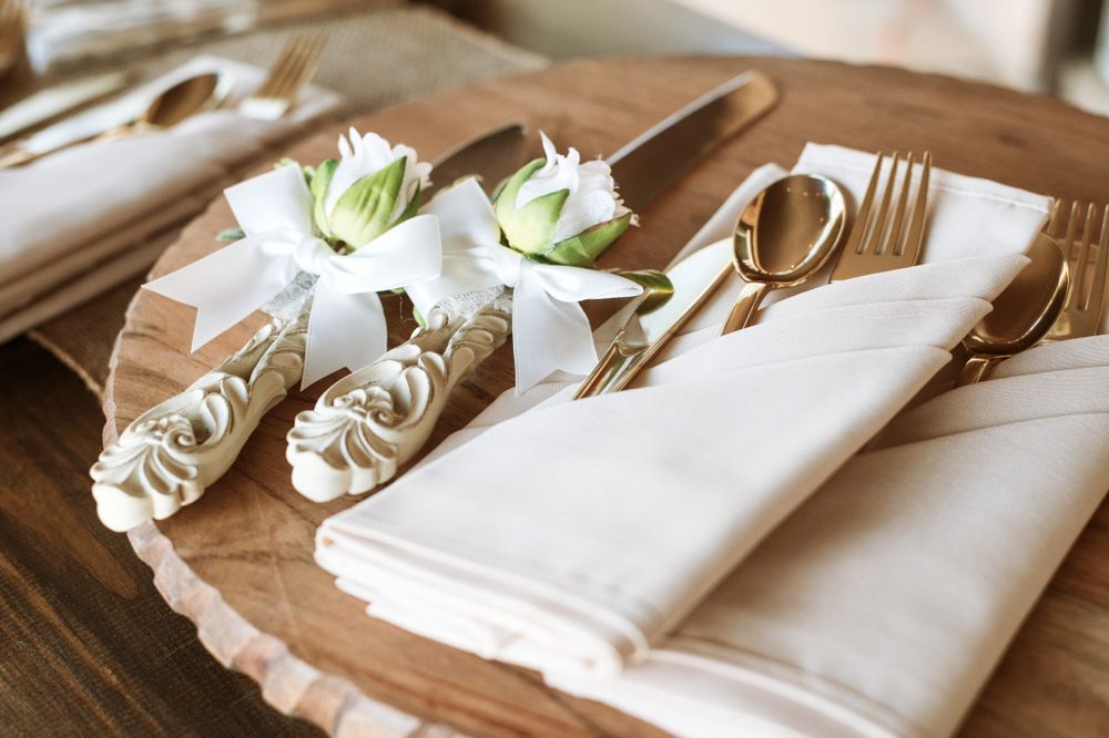 Elegant place setting with white napkins and flowers arranged on wooden charger plates.