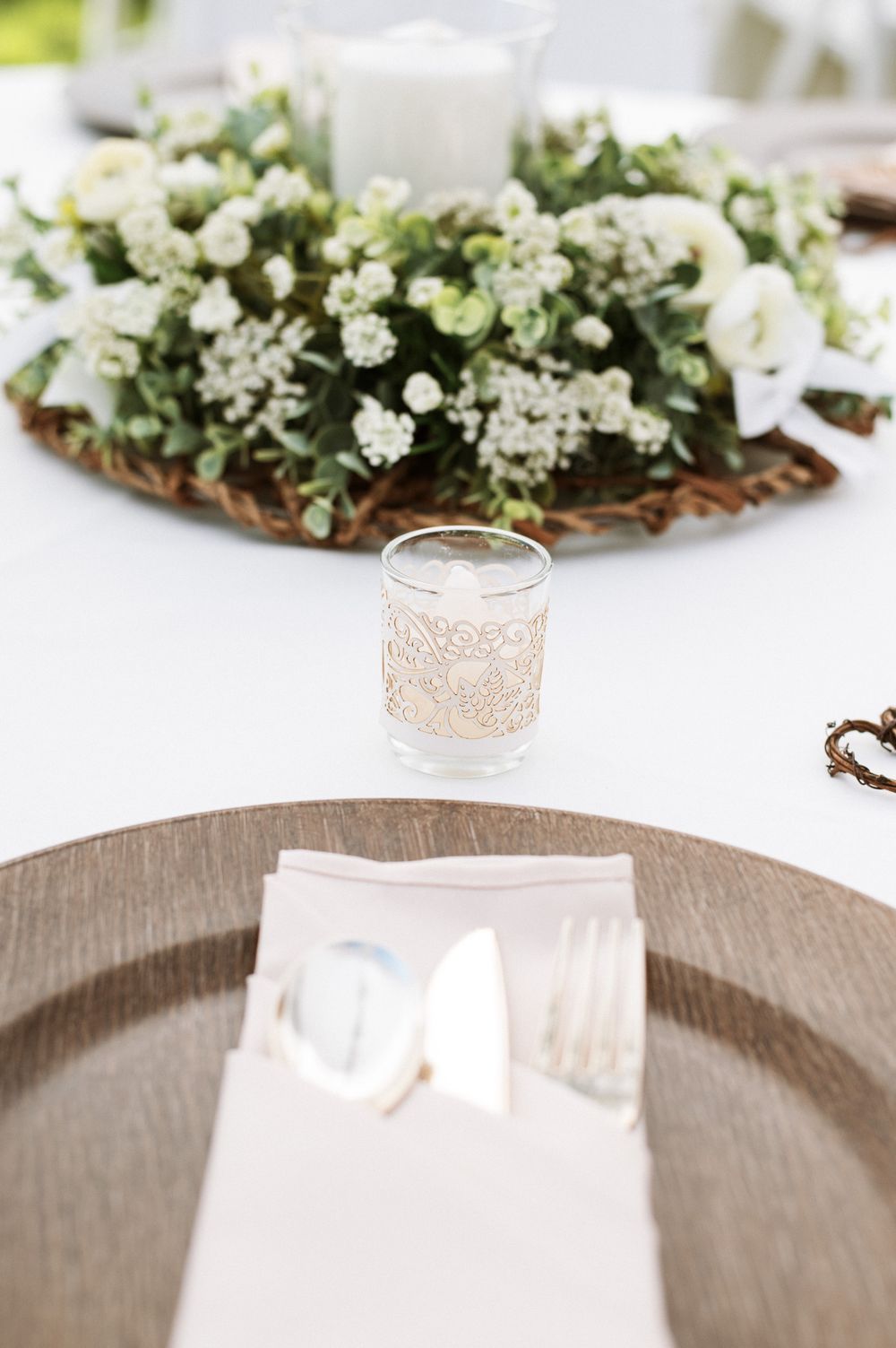 White floral centerpiece with delicate baby's breath on rustic wooden charger plate.