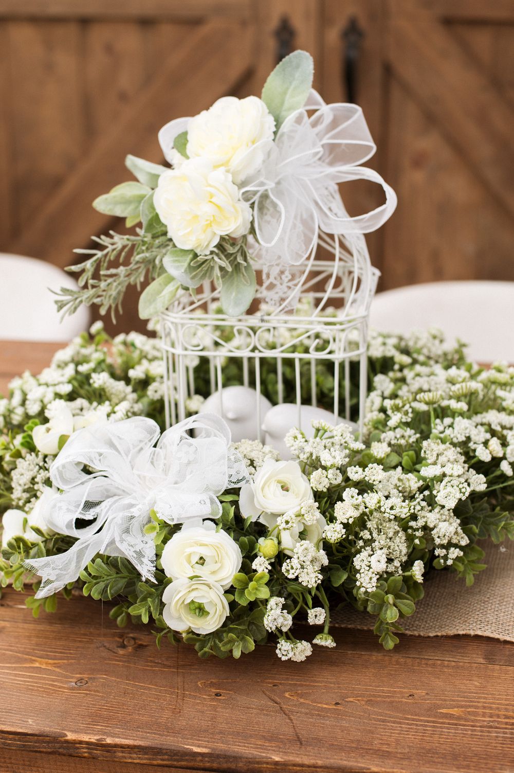 Decorative white birdcage adorned with roses, baby's breath, and ribbons as wedding centerpiece.