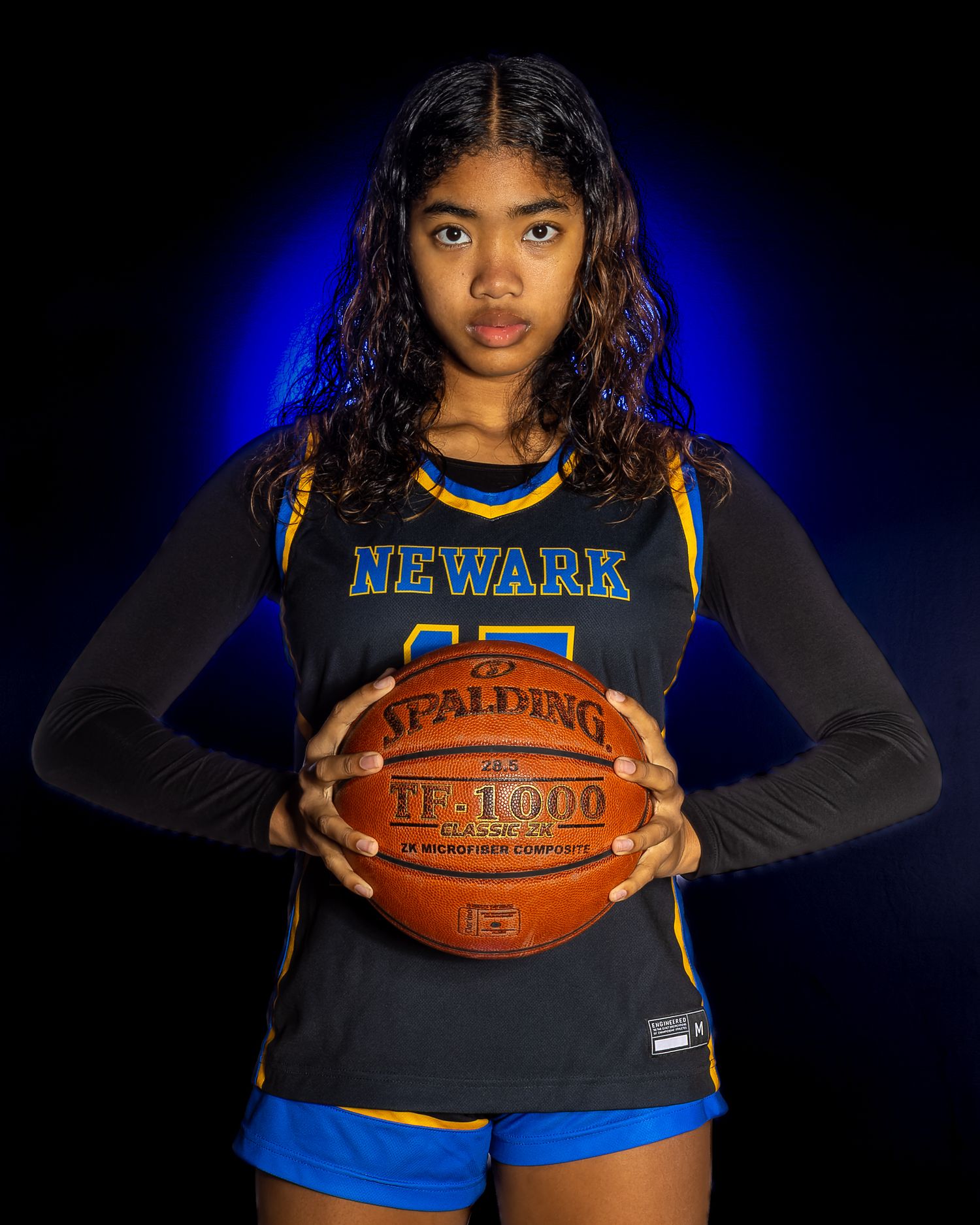 High school basketball player in Newark uniform holds Spalding basketball against blue backdrop.