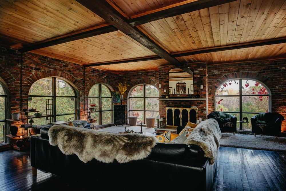 Luxurious bedroom with wooden ceiling beams, arched windows, and cozy fur throws overlooking a scenic mountain view.