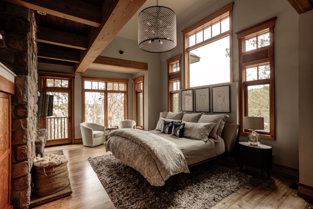 Modern rustic master bedroom featuring exposed beams, large windows, and a plush king bed with mountain views.