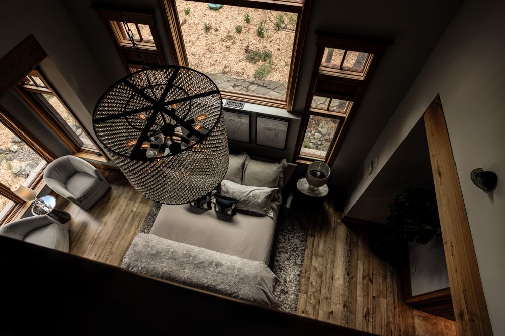 Aerial view of a cozy living space with industrial chandelier, rustic wood floors, and large windows.