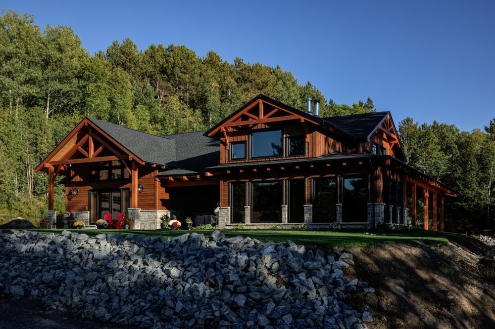 Panoramic view of a rustic log cabin lodge nestled among trees on a sunny day.