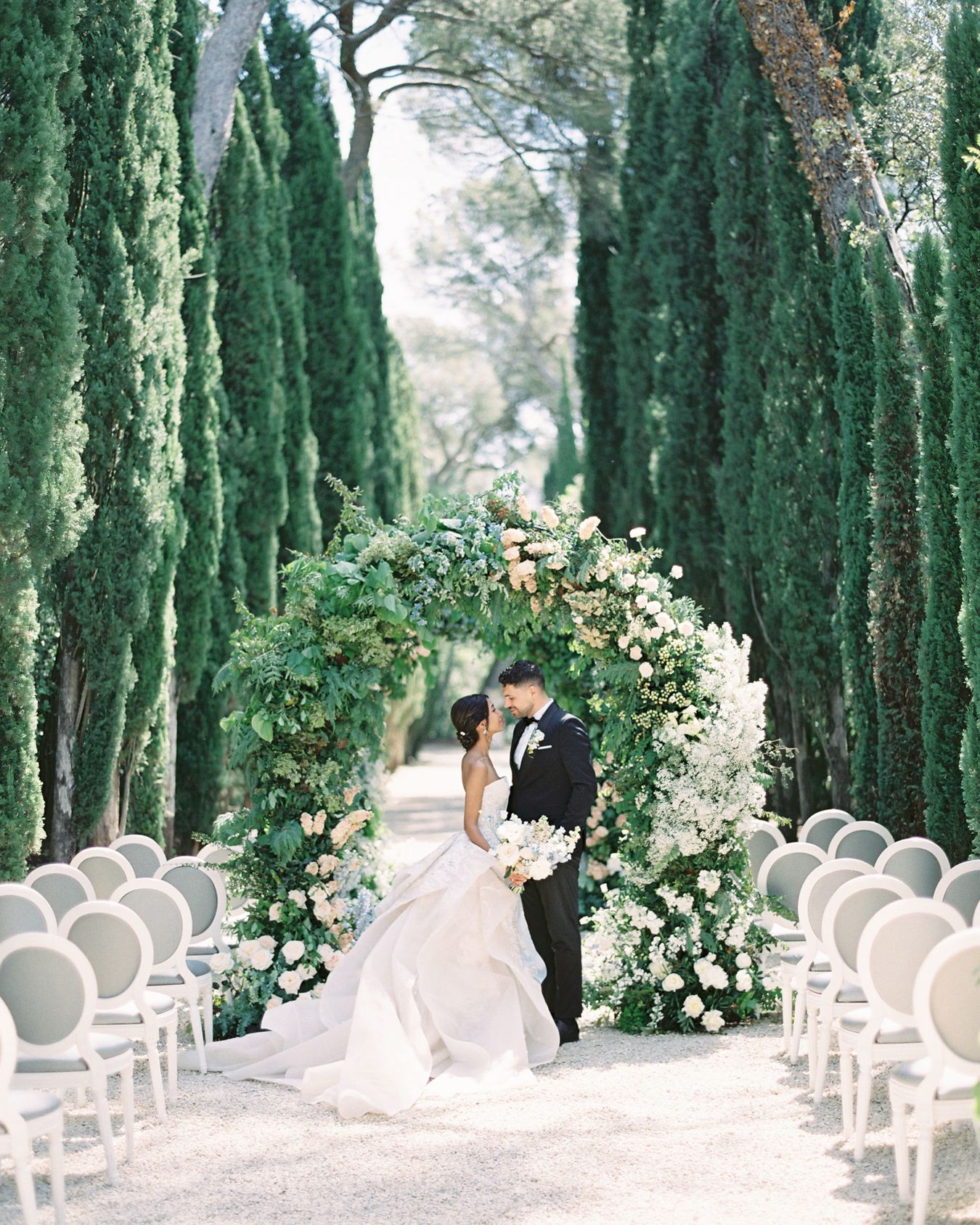 Romantic wedding ceremony setting with floral arch between rows of cypress trees.