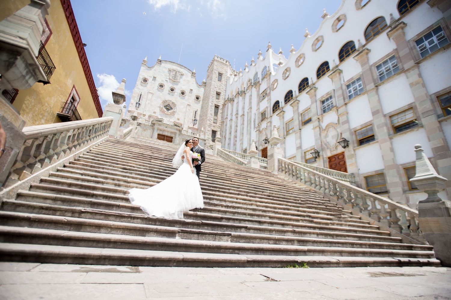 Wedding dress flowing on grand white stone staircase of historic building.