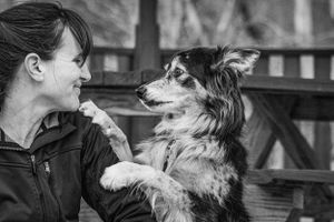 Black and white photo of a smiling woman interacting affectionately with her Border Collie mix dog outdoors. Photo by Xenophon Photography