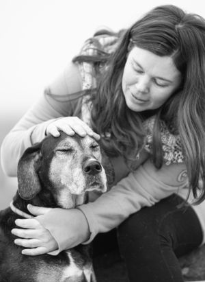 Young woman smiling while gently petting her elderly dog's head in a black and white portrait. Canine Photographer in Maine