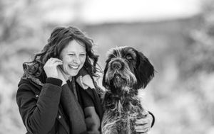 Smiling woman holding her Wirehaired Pointing Griffon dog outdoors in black and white portrait photo. Pet Photographer in Maine