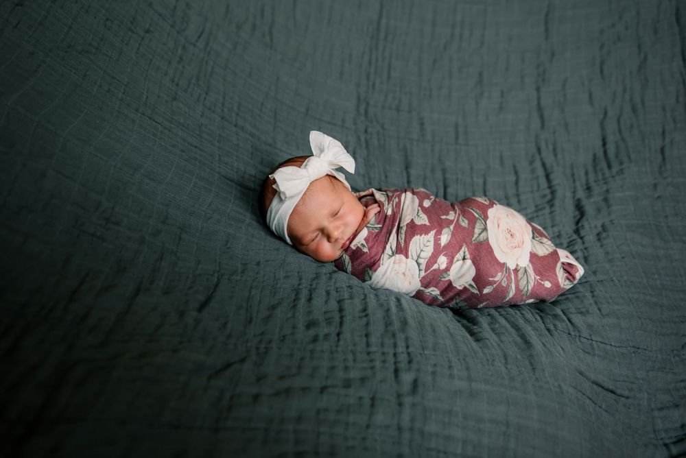 Newborn sleeping peacefully on textured green bedding in floral swaddle.