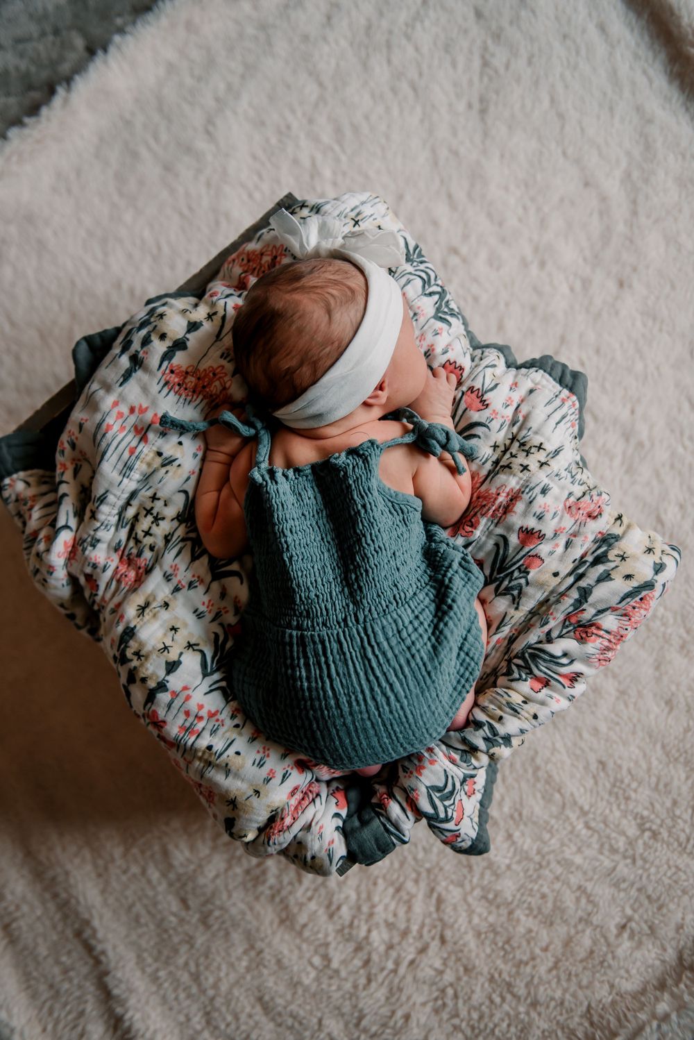 Newborn wearing teal knit outfit resting on white floral blanket.