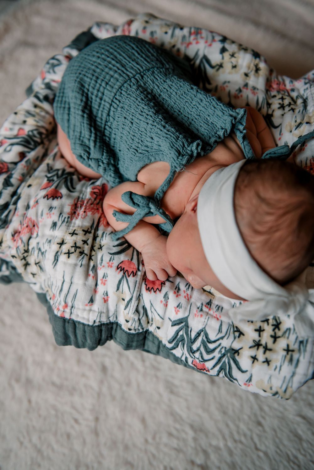Baby wrapped in teal muslin blanket resting on floral print fabric.