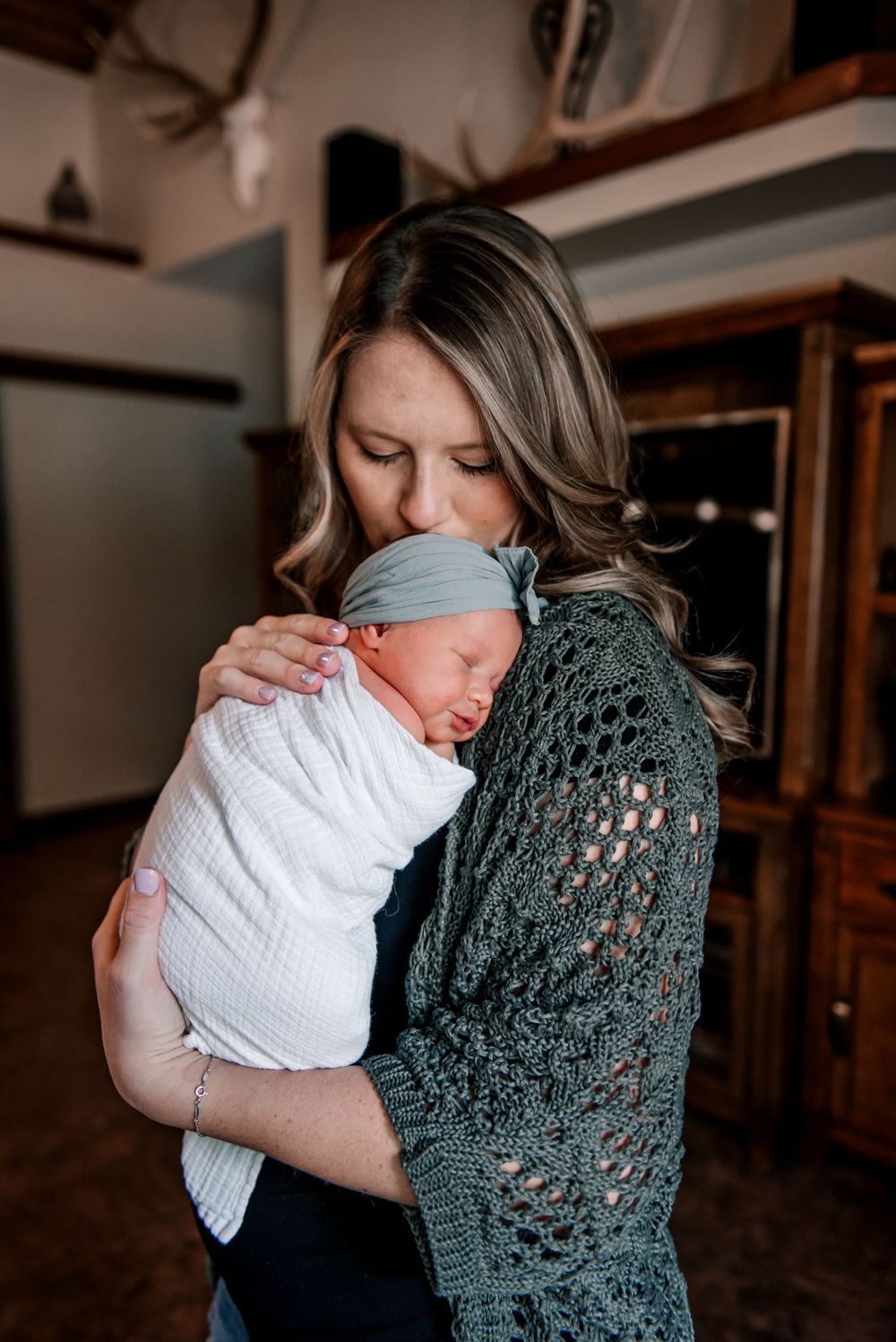 Tender family moment with baby wearing white onesie and teal hat.