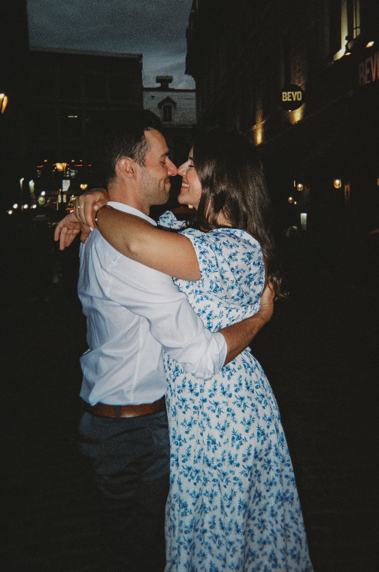 A couple dances together on a dark city street illuminated by ambient lighting.