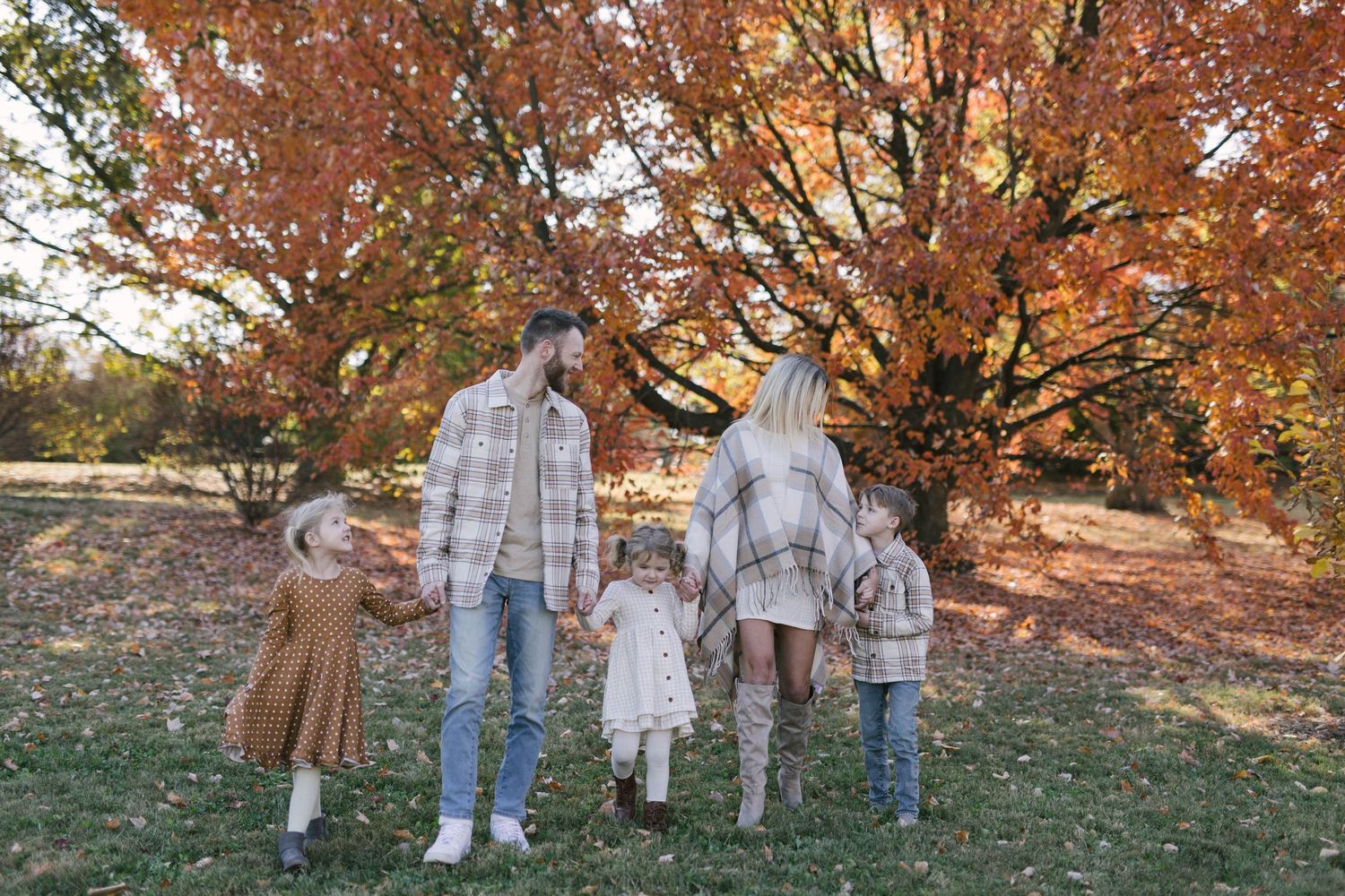 A family poses together under autumn trees with orange and red leaves falling around them.
