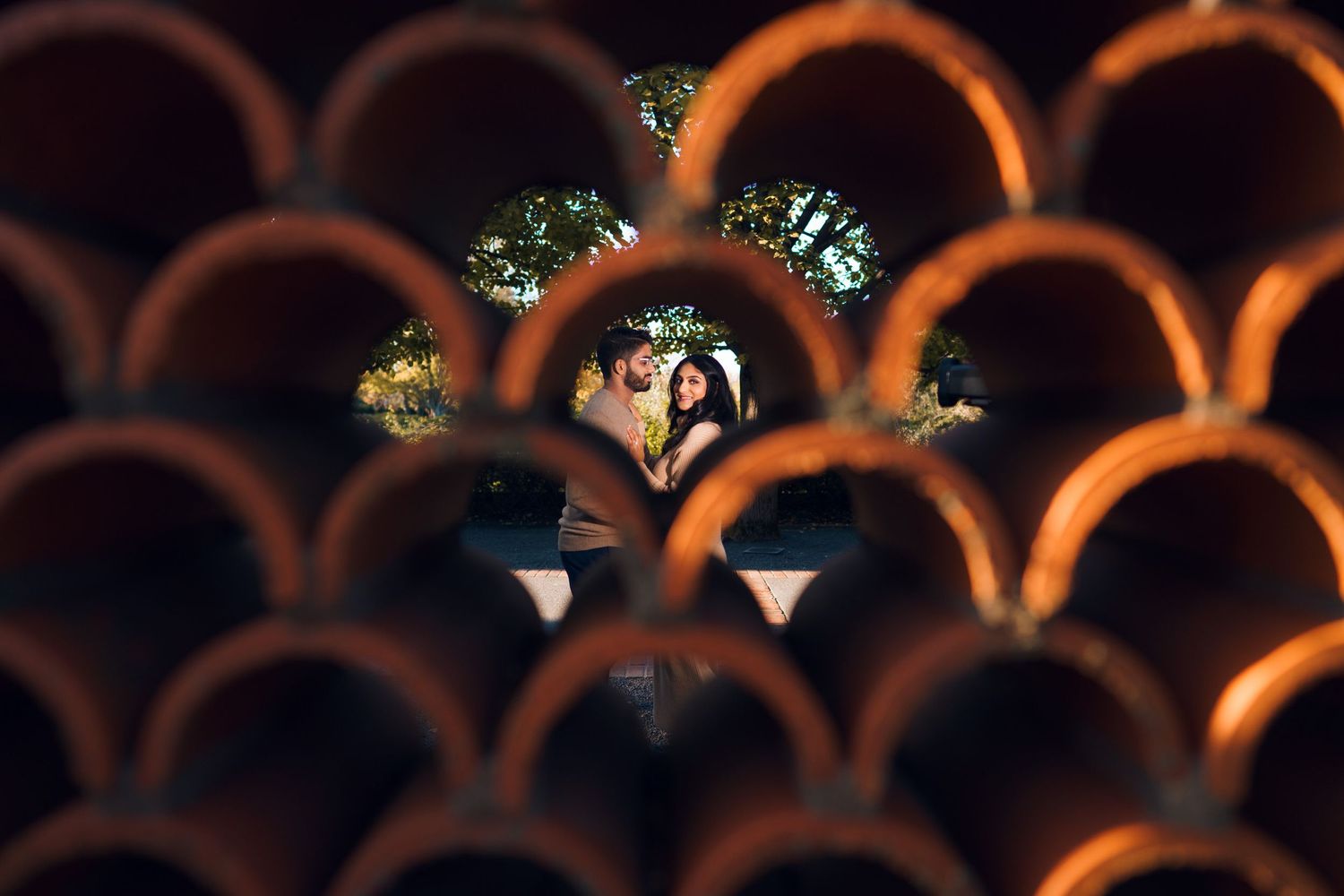 Couple's affectionate hug, their gaze framed by a wall of stacked Spanish tiles, blending love and artistry.