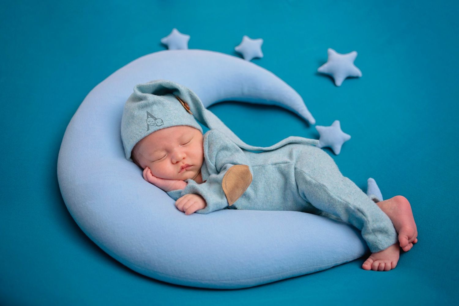 Newborn sleeping peacefully on blue crescent moon cushion with stars.