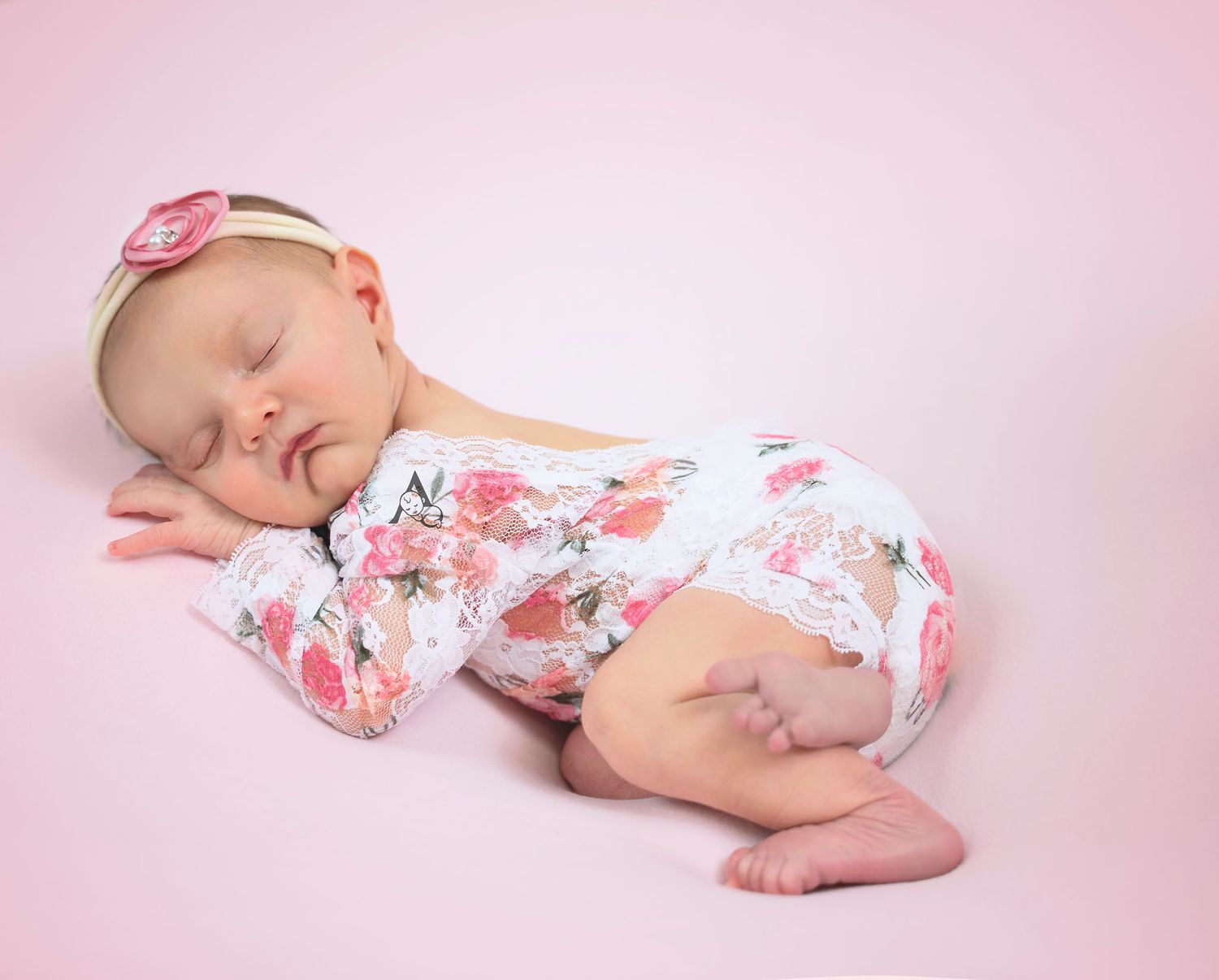 Sleeping newborn in floral outfit on pink backdrop during professional photo session.