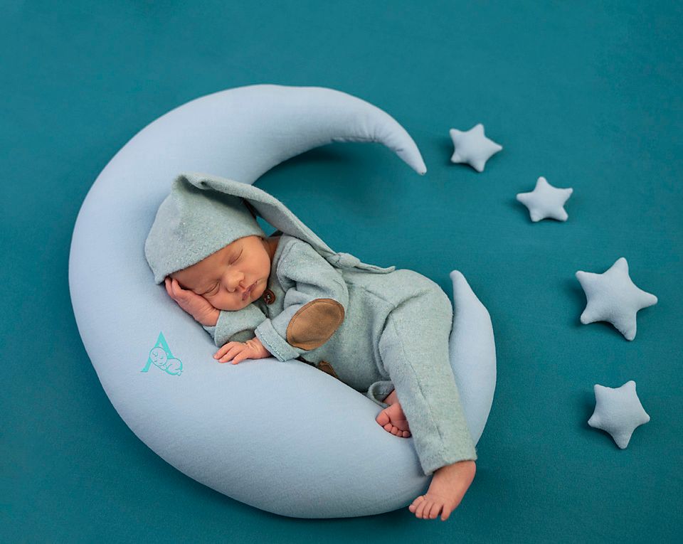 Sleeping newborn on teal background with crescent moon pillow and white stars.