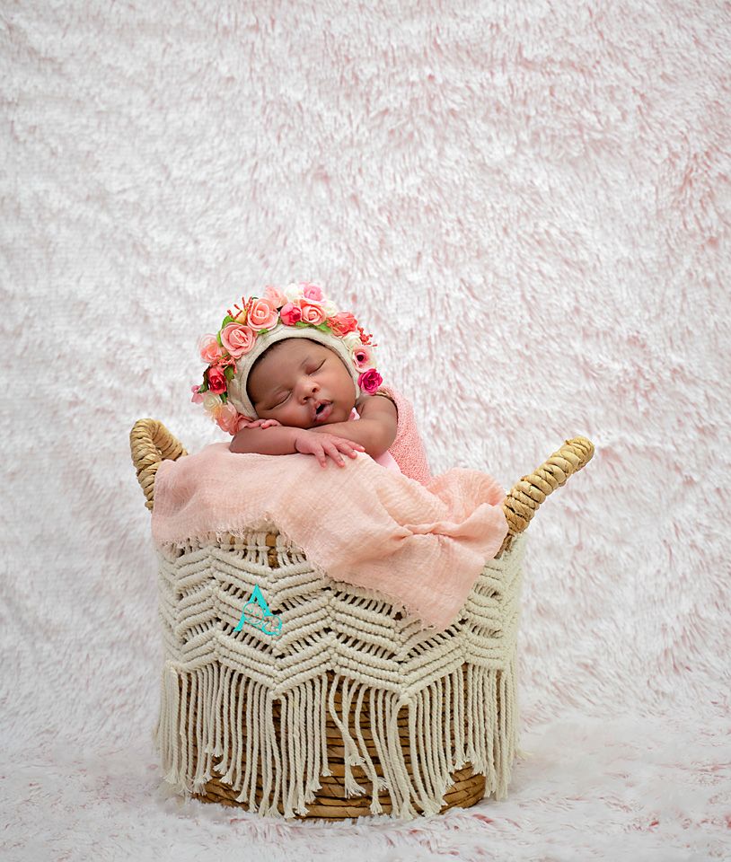 Sleeping newborn in pink outfit rests in decorative macrame basket.