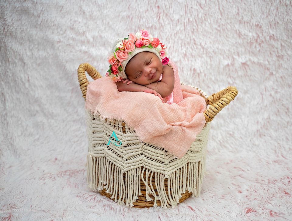 Newborn sleeping in macrame basket with pink blanket and floral crown.