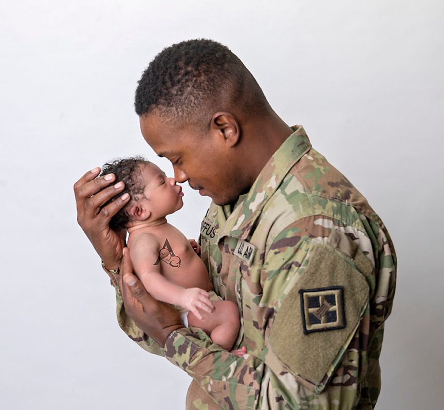 Military service member in camouflage uniform tenderly holds sleeping newborn.