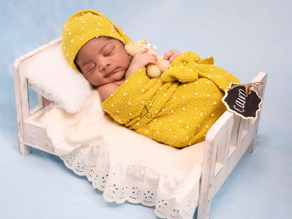 Sleeping newborn in yellow knit outfit on white lace bed.