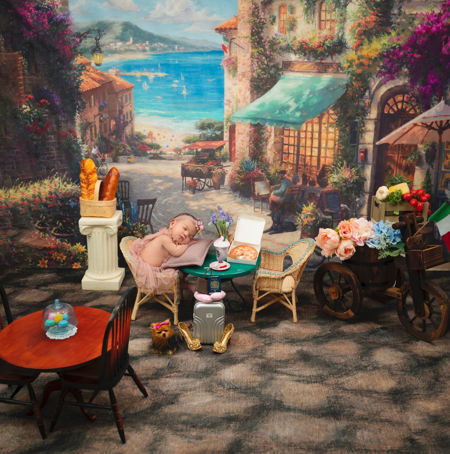 Scenic Mediterranean coastal town backdrop with outdoor cafe furniture and floral decorations.