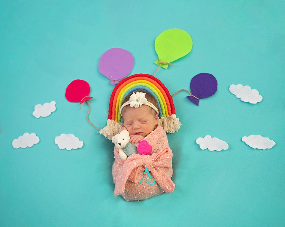 Sleeping newborn with rainbow decoration and colorful balloons on turquoise background.
