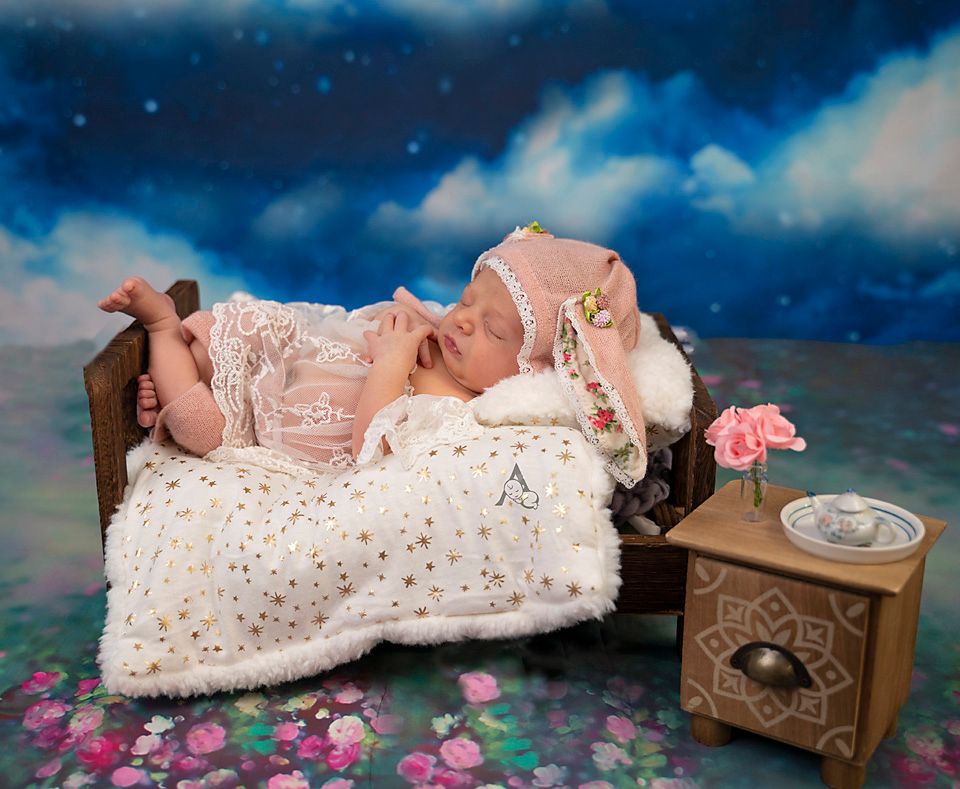 A vintage-styled newborn portrait with an antique bed, lace dress, and floral accents against a dreamy backdrop.