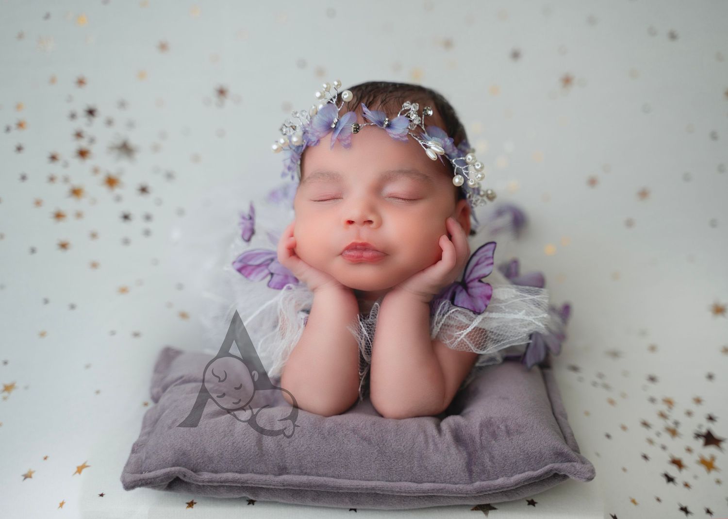 Sleeping newborn wearing floral crown posed on purple pillow with delicate styling.