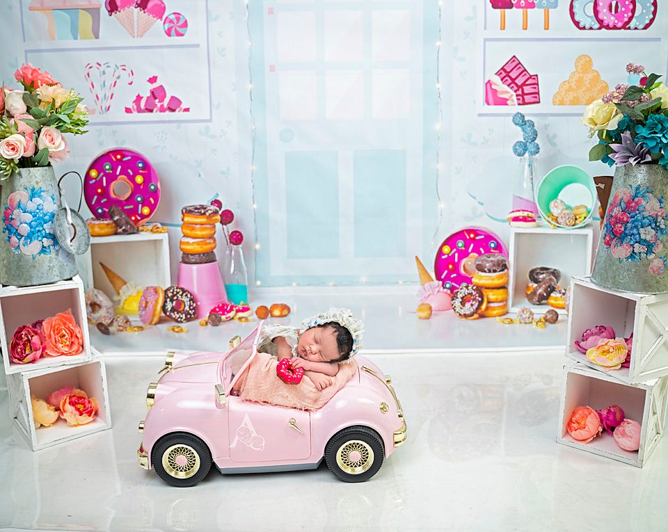 Baby sleeping in pink toy car surrounded by whimsical pastel decorations and toys.
