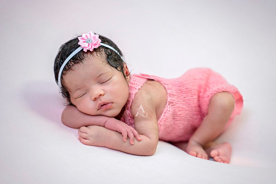 Sleeping baby wearing pink outfit and floral headband on white background.