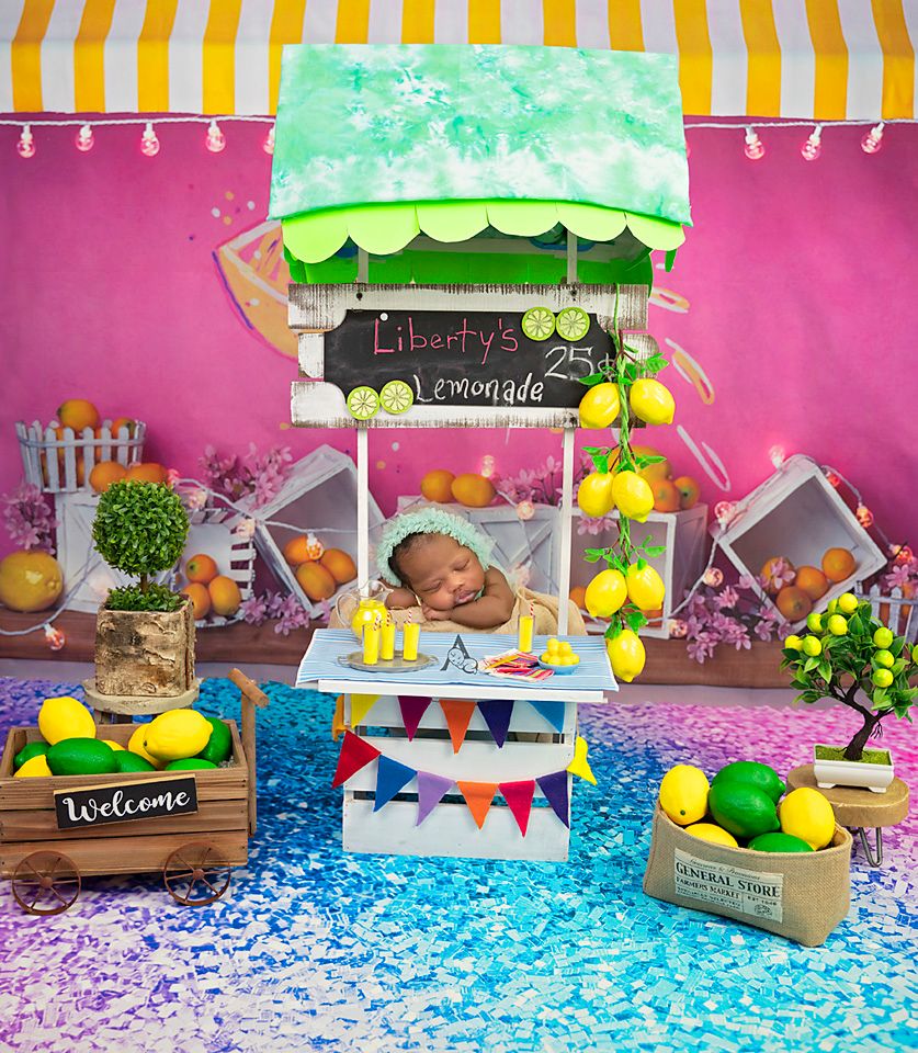 Baby sleeping at colorful lemonade stand setup with fruit decorations.