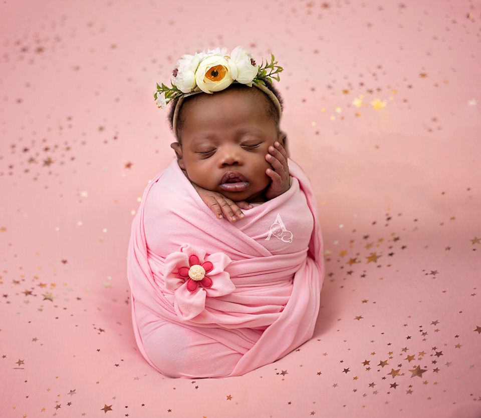 Dreamy newborn portrait with floral crown wrapped in pink fabric against rose background.