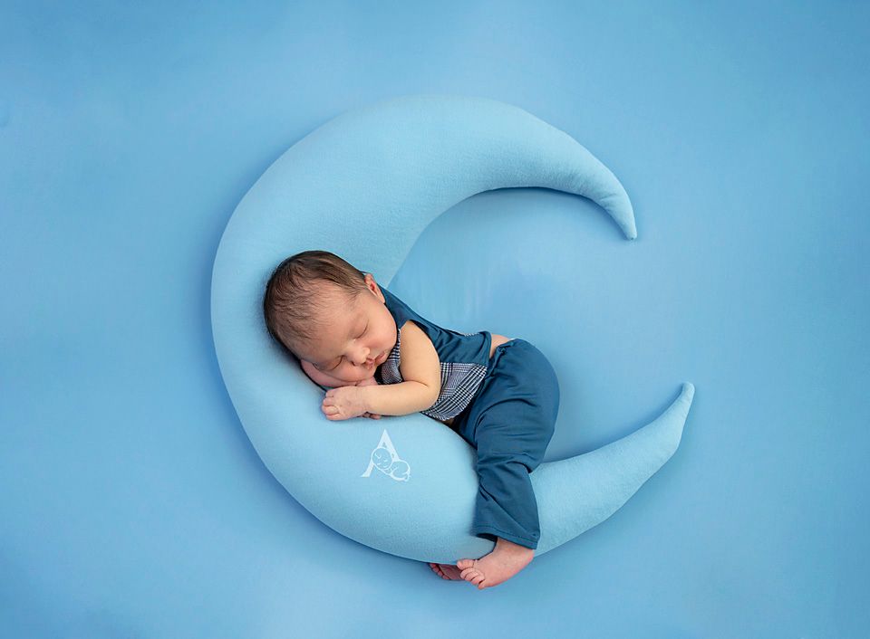 Peaceful sleeping newborn posed on blue crescent moon prop.