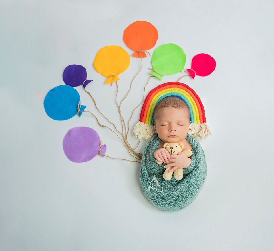 Whimsical newborn photo with colorful balloon props and rainbow accent.
