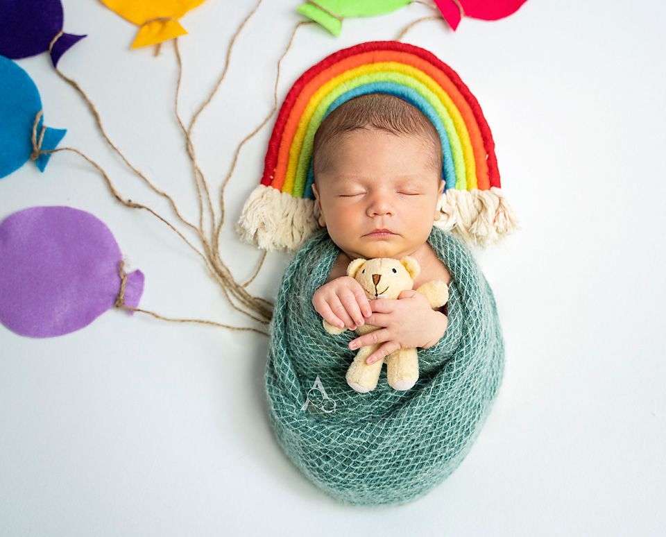 Sweet newborn portrait with rainbow prop and colorful balloon decorations.