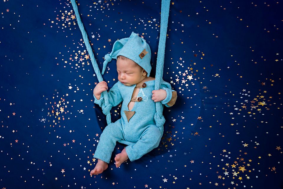 Dreamy newborn portrait in blue outfit with sparkle overlay effect.