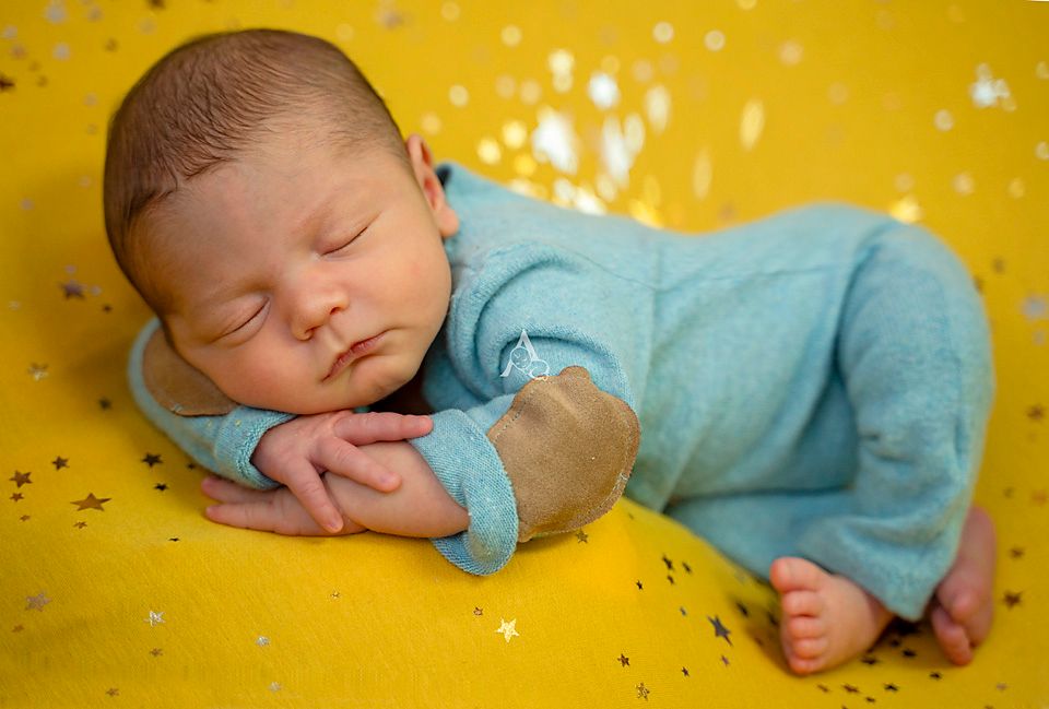 Sleeping newborn in light blue outfit resting on yellow background with sparkles.
