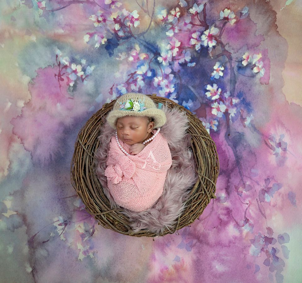 Artistic newborn portrait in woven nest with dreamy watercolor floral background.