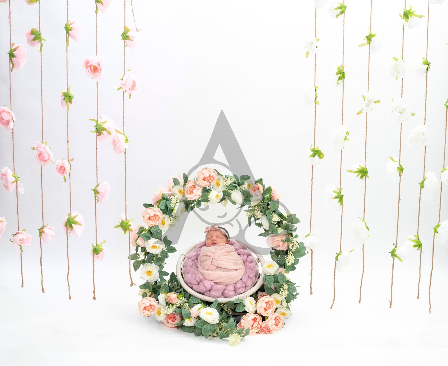 Floral wreath with pink roses and greenery against white background with hanging vine decoration.