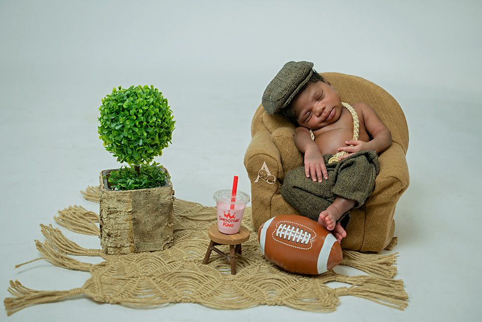 Creative newborn photo setup with football, topiary plant and rustic elements.